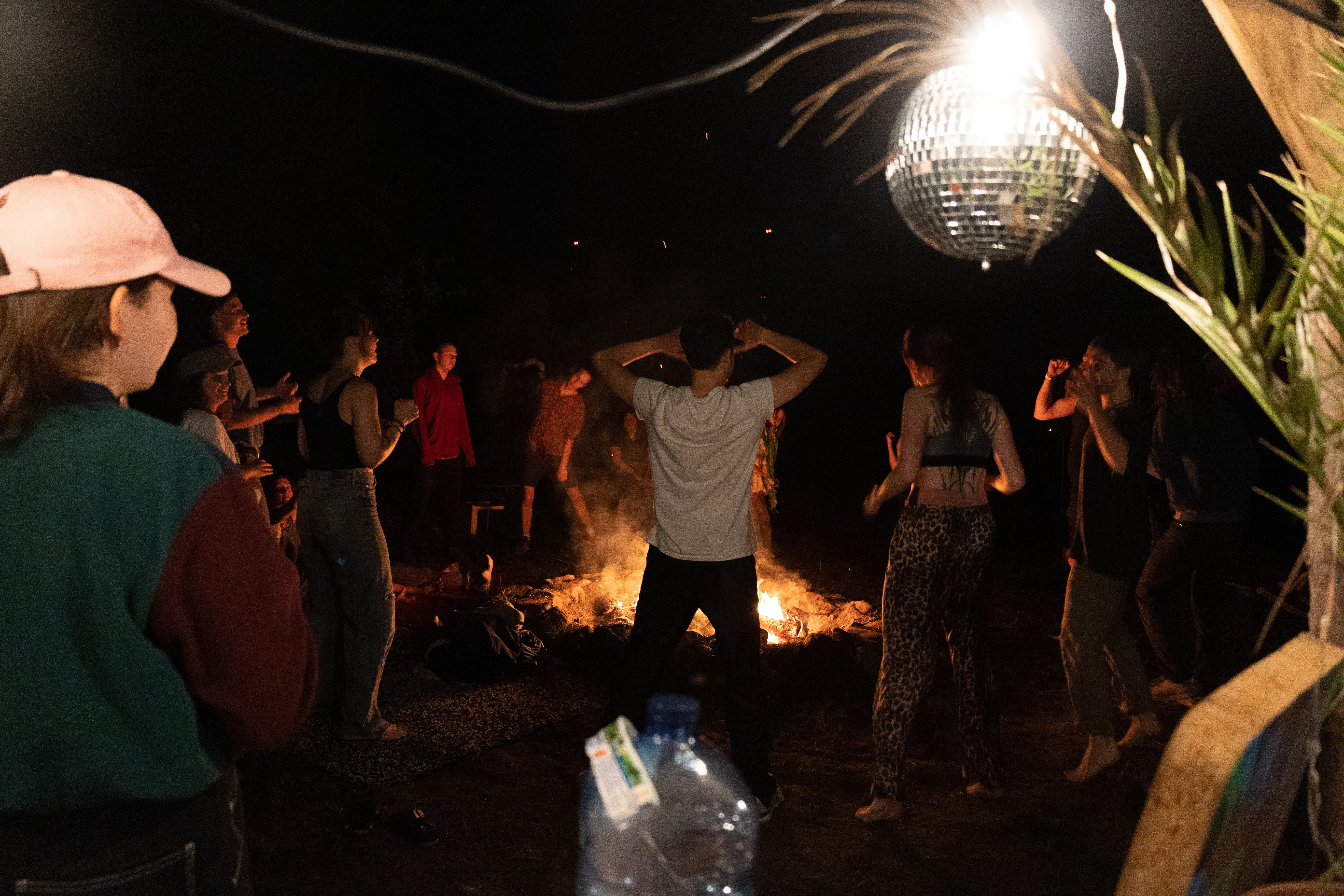 Menschen tanzen um ein Lagerfeuer. Oben rechts hänge eine Discokugel.